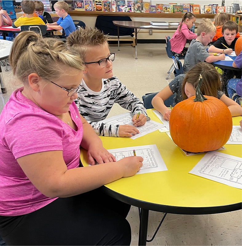 A group of children sitting at a table with a pumpkin in front of them