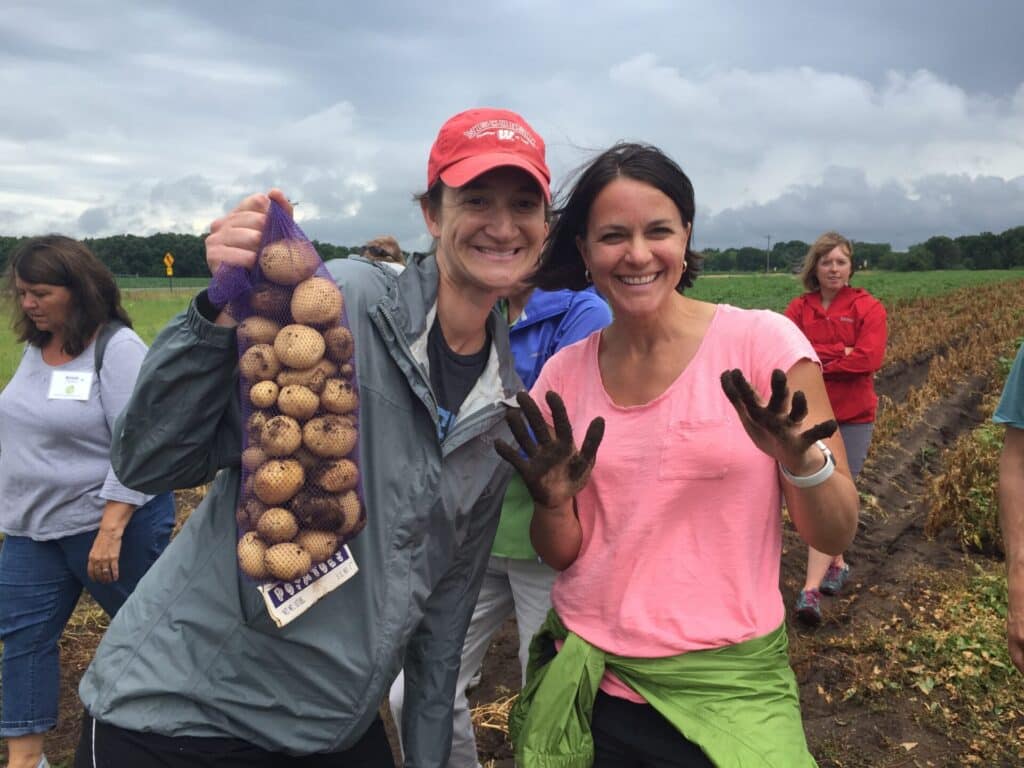 Two women holding potatoes in a field.