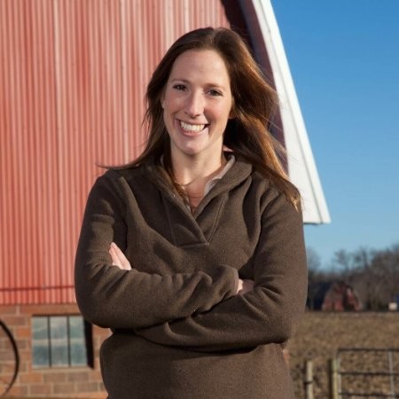 woman standing in front of a red barn outside with a brown sweater on