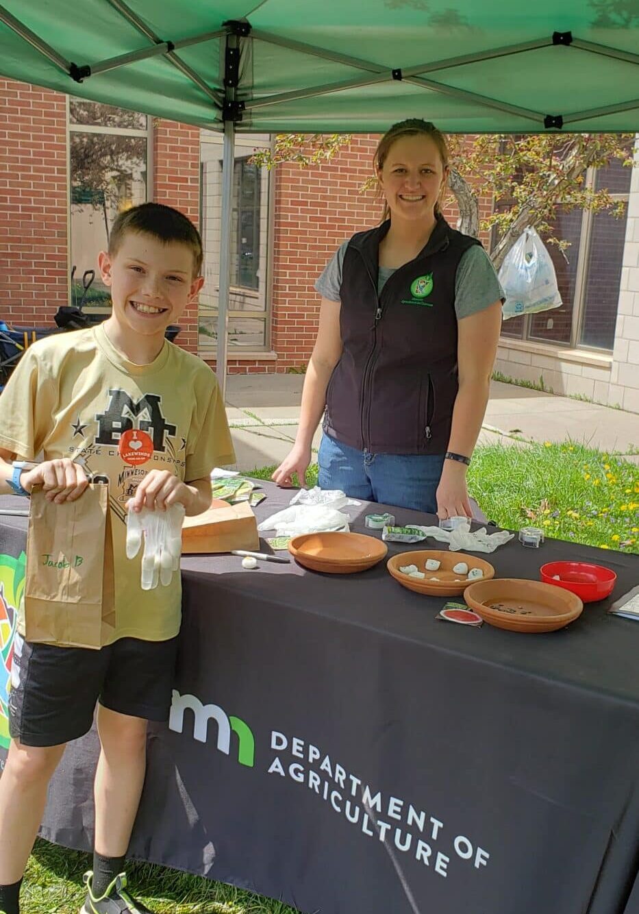 A Woman And A Boy Volunteer Next To A Table With Food On It