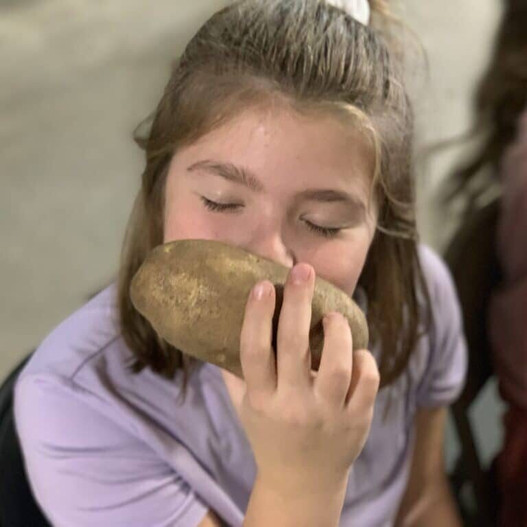 A Girl Is Eating A Potato In Front Of A Group Of People Encouraging Them To Make A Donation