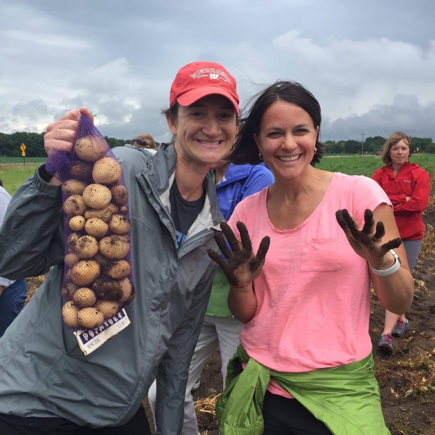 Two women holding potatoes in a field.